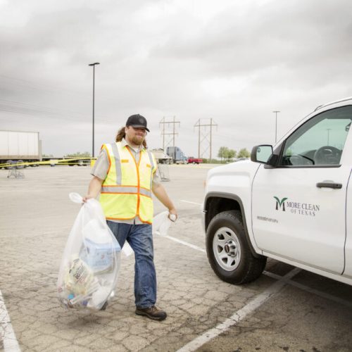 Texas Street Sweeping Service and Day Porter Services More Clean of Texas employee in high visibility vest carrying a bag of trash to company truck